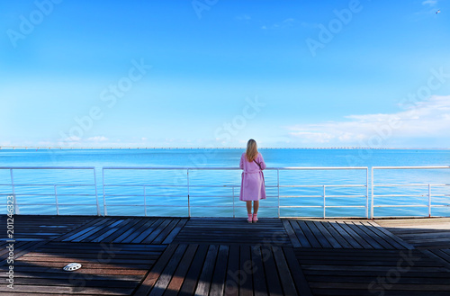 Young pretty woman standing alone on the pier near the sea