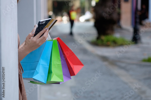 Cropped shot of shopping bag and smartphone with credit card on woman hands.
