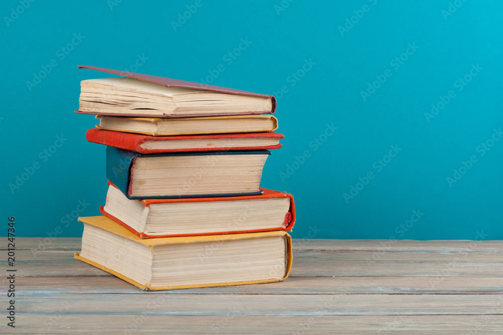 Book stacking. Open hardback books on wooden table and blue background. Back to school. Copy space for ad text Book stacking. Open hardback books on wooden table and blue background. Back to school. Copy space for ad text