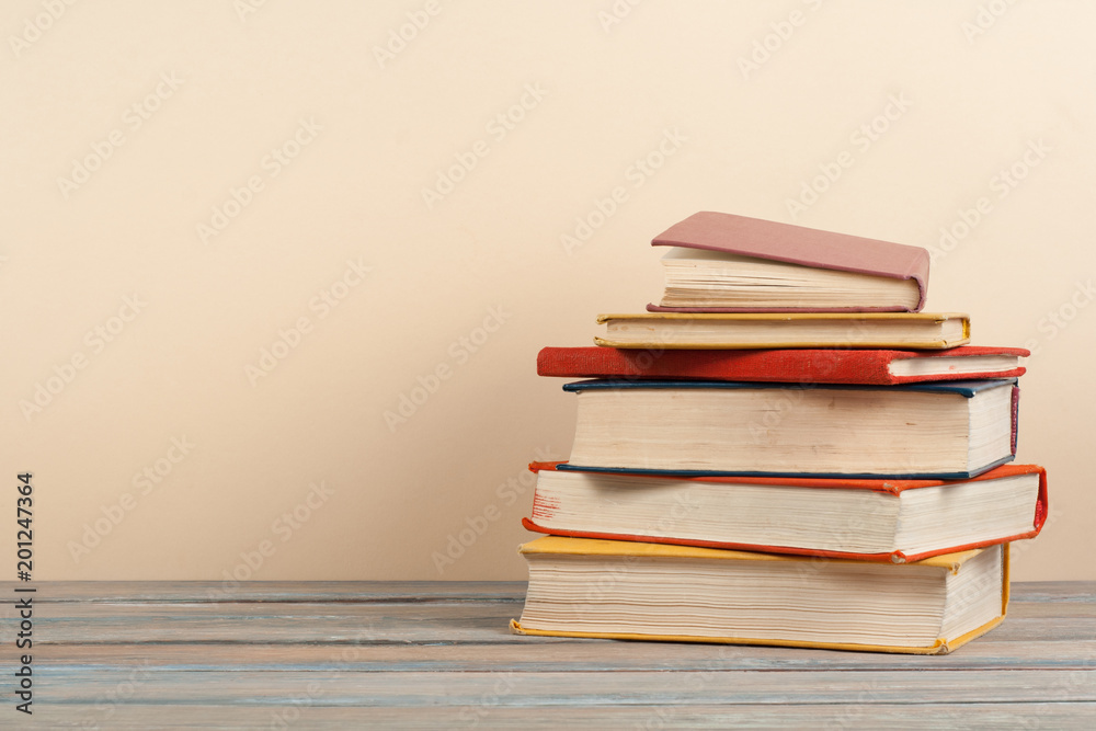 Book stacking. Open hardback books on wooden table and beige background. Back to school. Copy space for ad text. Book stacking. Open hardback books on wooden table and beige background. Back to school. Copy space for ad text.