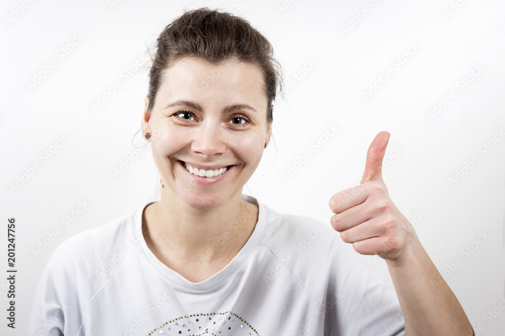 Portrait of attractive brunette smiling girl holding her thumb up against white background. Portrait of attractive brunette smiling girl holding her thumb up against white background.