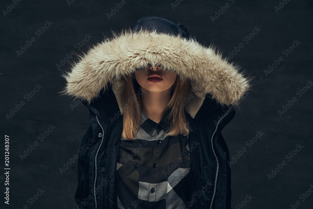 Portrait of a sexy blonde girl in a winter jacket and fleece shirt, standing in a studio.