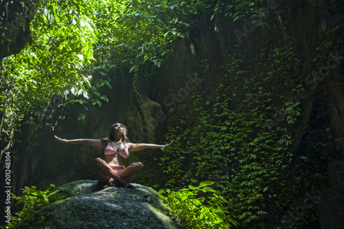 young beautiful Asian woman practicing Yoga posing sitting in meditation  position over a stone in a stunning natural landscape full of vegetation