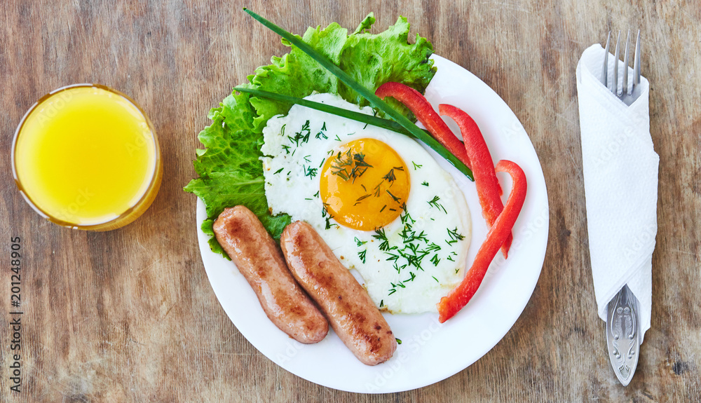Tasty breakfast on white plate consisting from egg sausages vegatables orange juice. Top view Tasty breakfast on white plate consisting from egg sausages vegatables orange juice. Top view