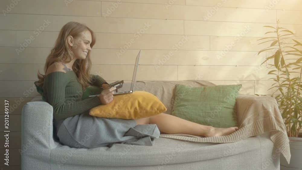Beautiful young woman using a laptop, holding a credit card and smiling while doing shopping online at home Beautiful young woman using a laptop, holding a credit card and smiling while doing shopping online at home