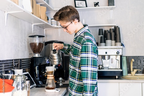 Barista with glasses in a green shirt prepares coffee in the cafe