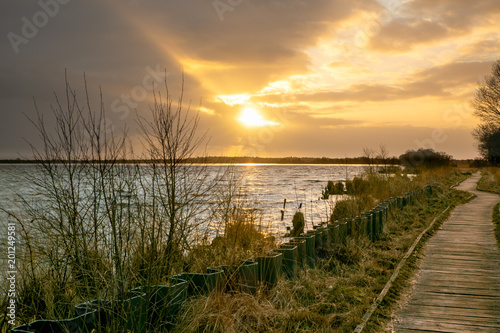 Sunset over the big bog lake. A boardwalk leads through the moor on the shore of the lake - photographed near Eversmeer, Germany