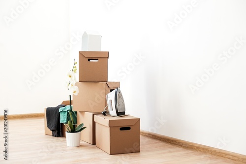Cardboard boxes with things are on the floor in an empty room with white walls