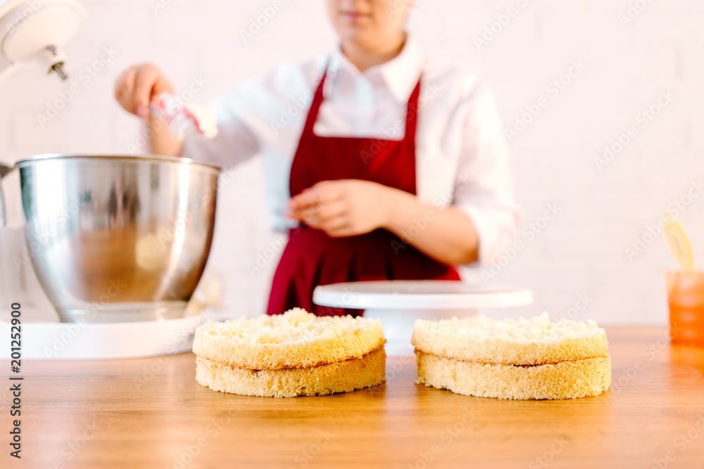 Pastry chef at the wooden table in the kitchen preparing a cake