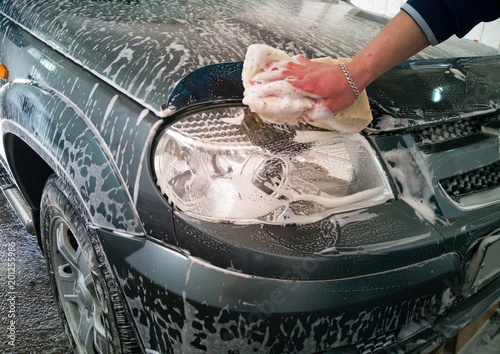 Car wash. The worker washes the right headlight with a sponge and soap foam. photo