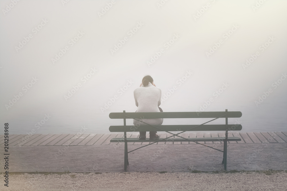 Rückansicht Junge Frau sitzt betrübt und einsam auf einer Bank im Nebel