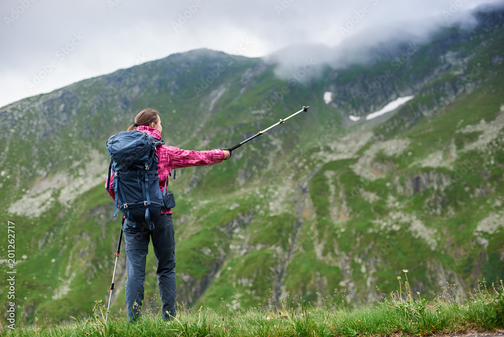 Rear view shot of a female backpacker standing on top of a hill pointing away with her trekking pole copyspace leadership achieving sports active living recreation nature environment camping.