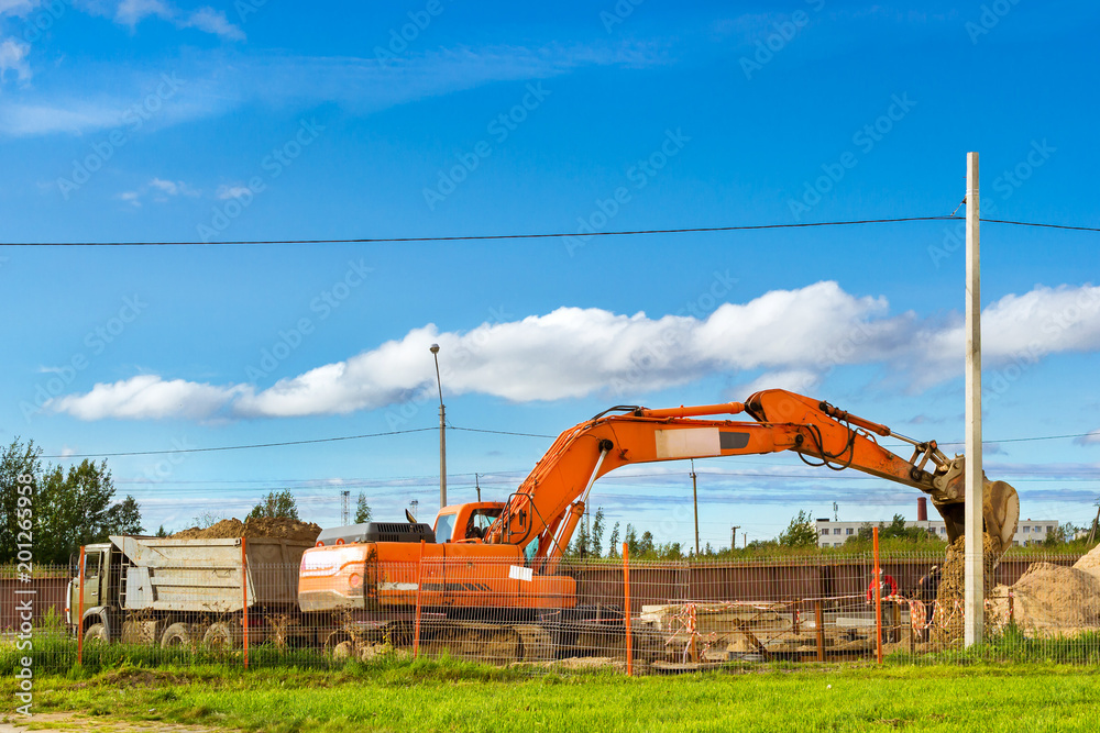 Excavator bucket loads heavy truck with ground on construction of highspeed road around Krasnoe Selo. Heavy industry machinery equipment for excavation works. St.Petersburg, Russia Excavator bucket loads heavy truck with ground on construction of highspeed road around Krasnoe Selo. Heavy industry machinery equipment for excavation works. St.Petersburg, Russia