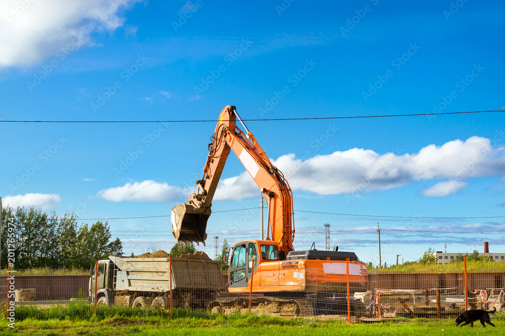 Excavator bucket loads heavy truck with ground on construction of highspeed road around Krasnoe Selo. Heavy industry machinery equipment for excavation works. St.Petersburg, Russia Excavator bucket loads heavy truck with ground on construction of highspeed road around Krasnoe Selo. Heavy industry machinery equipment for excavation works. St.Petersburg, Russia