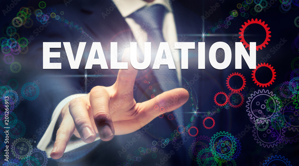 A businessman pressing a Evaluation business concept on a graphical display of cogs A businessman pressing a Evaluation business concept on a graphical display of cogs