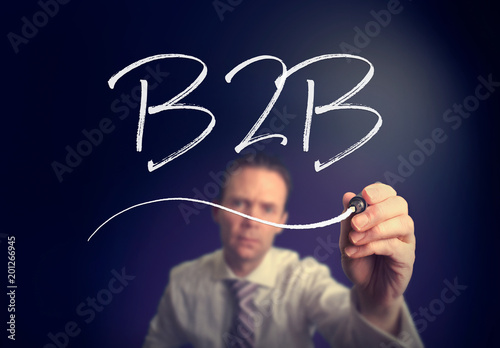 A businessman writing a B2B concept with a white pen on a clear screen.