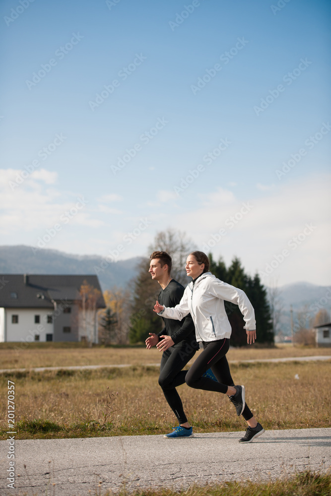 Young  veautiful couple runs on a path in park on autumn afternoon