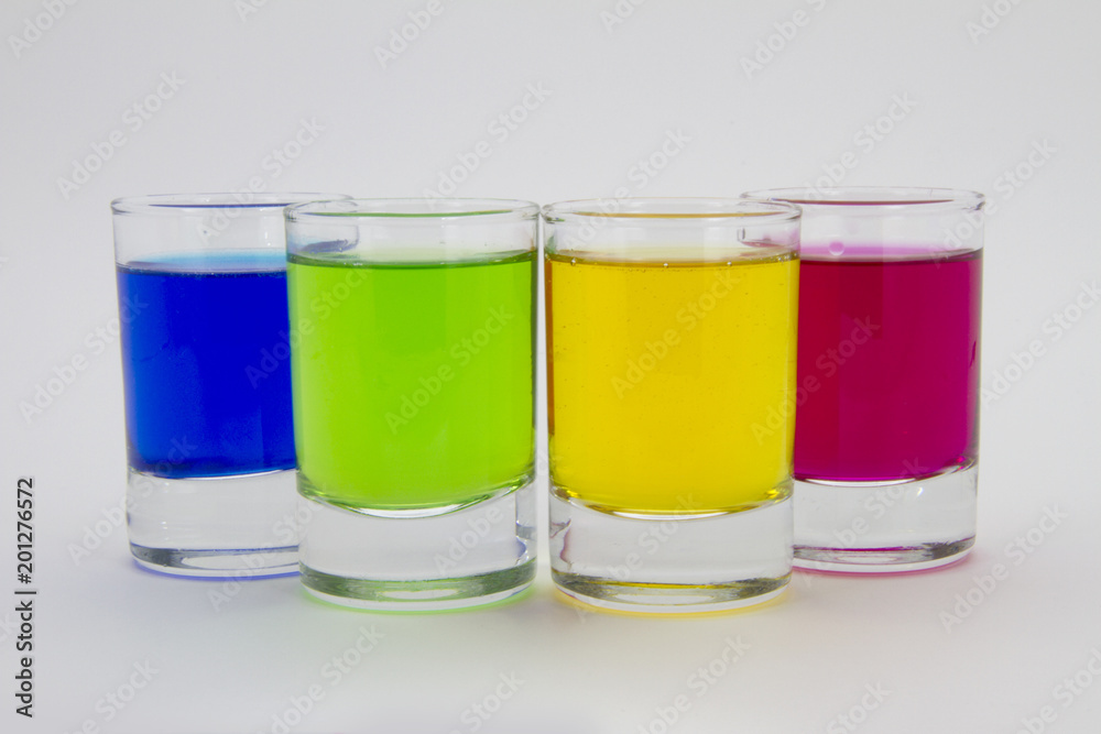 Multicolored glasses of different drinks. Party and holiday celebration concept. Four glasses with a blue, green, yellow and red drink. Isolated on white background. Multicolored glasses of different drinks. Party and holiday celebration concept. Four glasses with a blue, green, yellow and red drink. Isolated on white background.