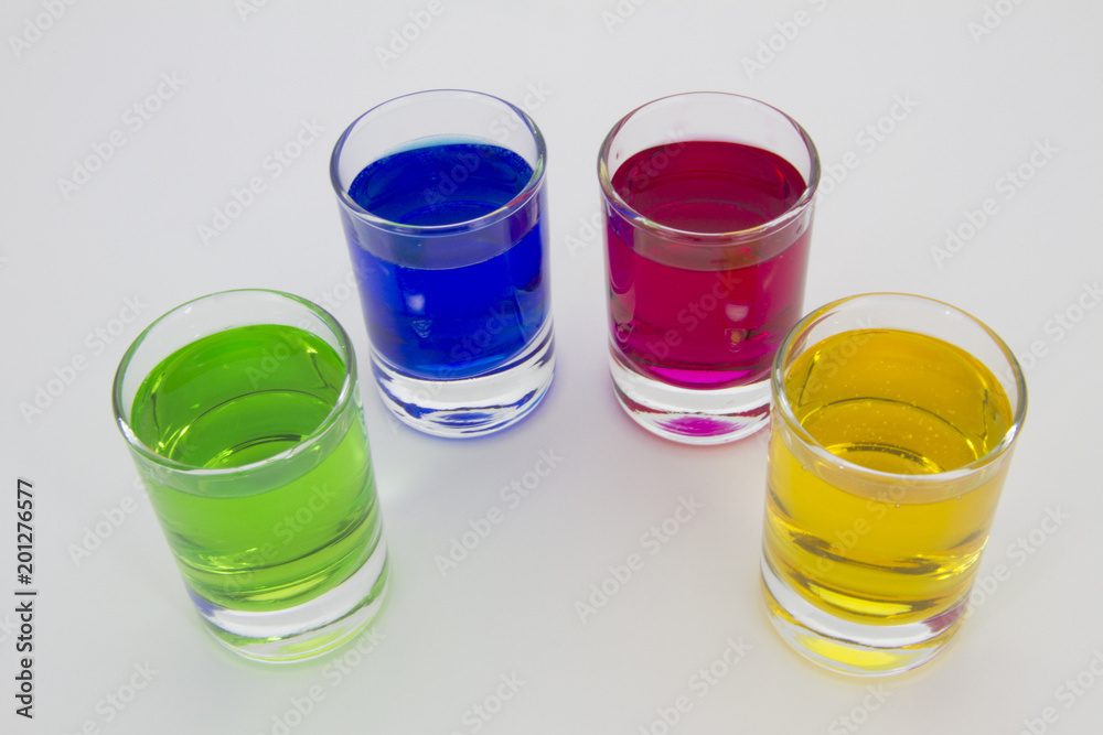 Multicolored glasses of different drinks. Party and holiday celebration concept. Four glasses with a blue, green, yellow and red drink. Isolated on white background. Multicolored glasses of different drinks. Party and holiday celebration concept. Four glasses with a blue, green, yellow and red drink. Isolated on white background.