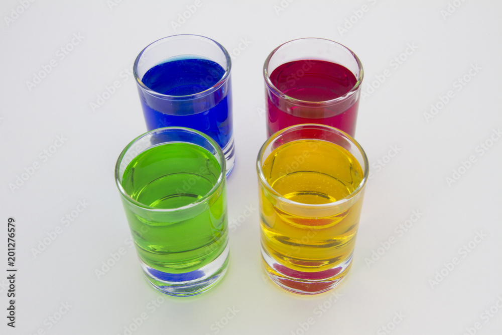 Multicolored glasses of different drinks. Party and holiday celebration concept. Four glasses with a blue, green, yellow and red drink. Isolated on white background. Multicolored glasses of different drinks. Party and holiday celebration concept. Four glasses with a blue, green, yellow and red drink. Isolated on white background.