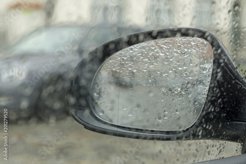 Drops of rain on the car window (glass) with a view of the exterior mirror and blurred background