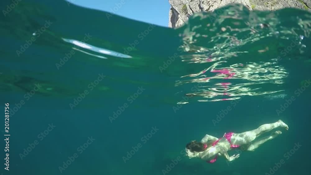 SLOW MOTION, HALF UNDERWATER: Cheerful young woman dives in deep sea on a beautiful summer day in Krabi. Carefree girl on relaxing holiday swims in picturesque scenery with clear sky and large cliffs.