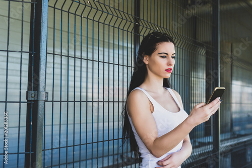 A young concentrated woman reads a message on the phone. The girl is holding the phone in hand. Female in a white T-shirt with sunglasses looks at the phone in consternation outside.