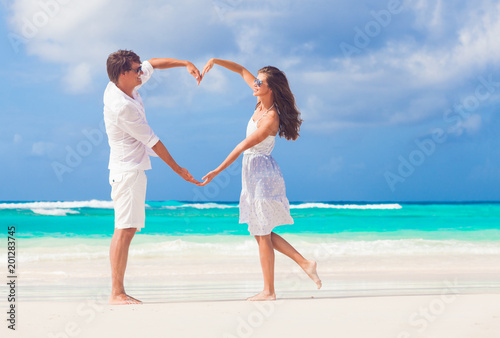 young happy couple in white making heart shape on tropical beach. honeymoon photo