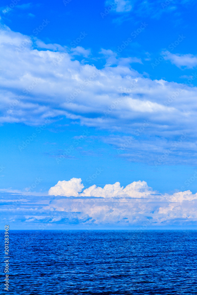 Panoramic view of ocean waters horizon line with dramatic cumulus thunderstorm cloudscape in blue sky background.