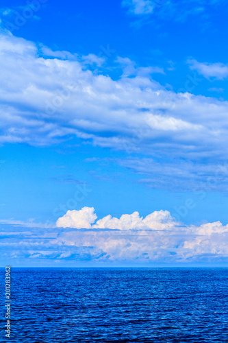 Panoramic view of ocean waters horizon line with dramatic cumulus thunderstorm cloudscape in blue sky background.