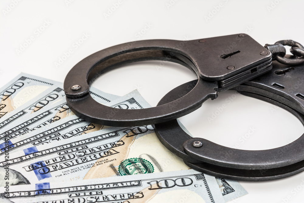 black metal handcuffs lying on the 100 dollars banknotes on a white background black metal handcuffs lying on the 100 dollars banknotes on a white background