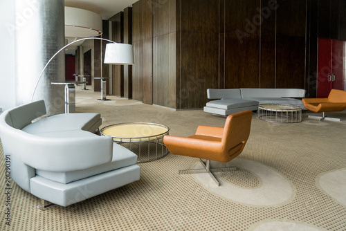 Modern hotel lobby with hallway or office lounge room. Interior with wood paneling, leather sofa and chairs, round metallic tables and floor lamp. Downtown workspace design concept photo