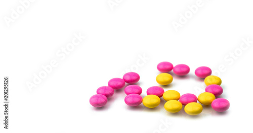 Pile of pink and yellow round sugar coated tablets pills isolated on white background with copy space. Colorful pills for treatment anti-anxiety, antidepressant and migraine headache prophylaxis.