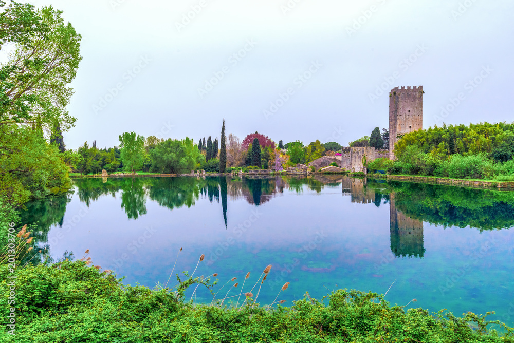 Garden of Ninfa, Italy - The exterior with reflection in a little lake of the medieval ruins in stone and flowers park. Province of Latina, Lazio region, central Italy. Garden of Ninfa, Italy - The exterior with reflection in a little lake of the medieval ruins in stone and flowers park. Province of Latina, Lazio region, central Italy.