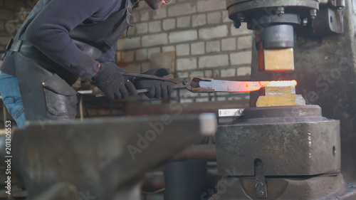 Man blacksmith forges the metal at the mechanical hammer