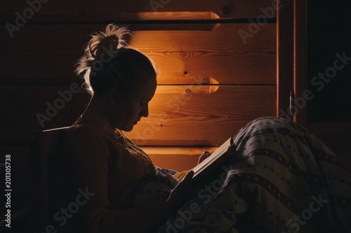 woman reading book in a bed, wooden cottage interior