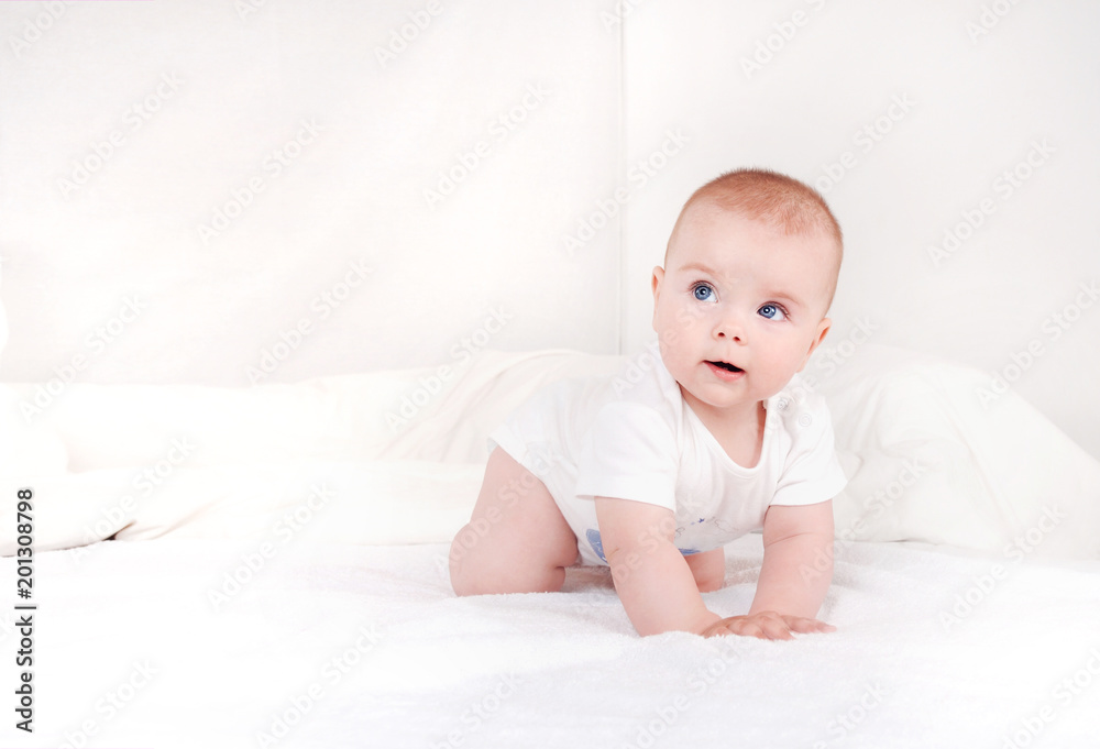 Portrait of sweet newborn infant crawlng on white bed serious looking away Portrait of sweet newborn infant crawlng on white bed serious looking away