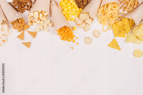 Quadro su tela Assortment of spicy colorful snacks in paper cones on white wooden board, top view food border with copy space for menu and advertising