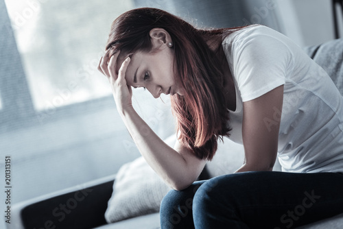 Depressive disorder. Charming dismal deplorable woman touching her forehead while regretting and looking down photo
