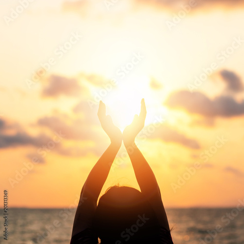 Summer sun June solstice concept and silhouette of happy young woman’s hands relaxing, meditating and holding sunset against warm golden hour sky on the beach with ocean or sea background photo