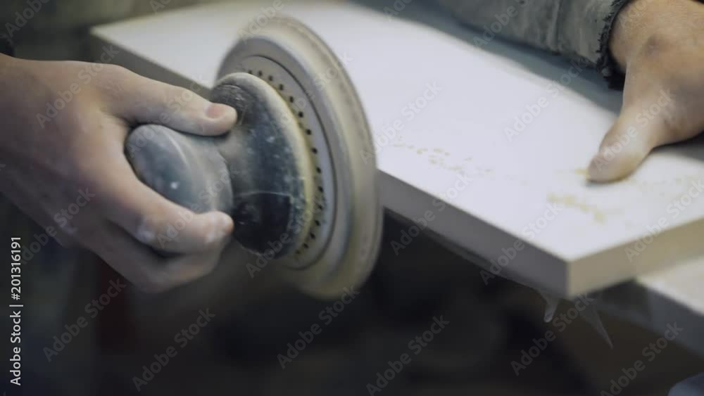 Working man with sander grinds wooden surface.
Working man with sander grinds wooden surface.