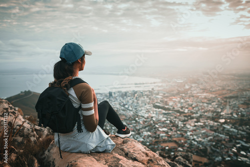 Young woman sitting on top of mountain overlooking city