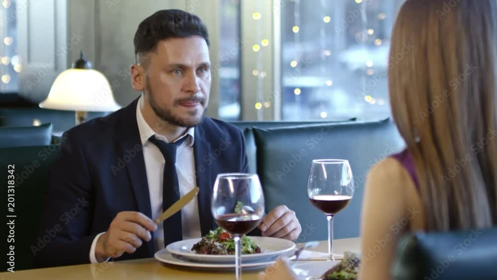 PAN of bearded man in suit and his unrecognizable girlfriend chatting and drinking wine on dinner date in restaurant PAN of bearded man in suit and his unrecognizable girlfriend chatting and drinking wine on dinner date in restaurant