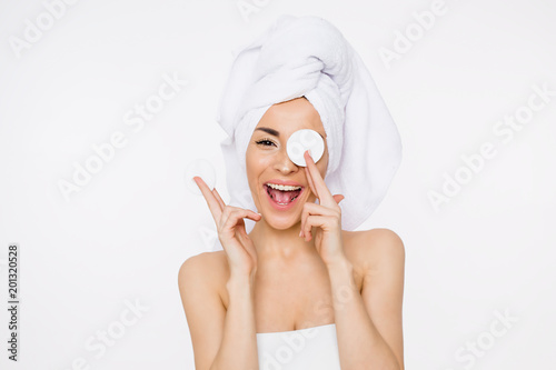 Removing makeup. Beauty and spa. A beautiful smiling woman with a towel on her head moisturizes or cleanses her face from makeup using cotton pads. Cosmetology. Women Health