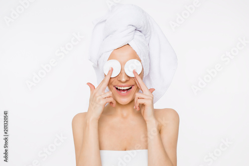 Removing makeup. Beauty and spa. A beautiful smiling woman with a towel on her head moisturizes or cleanses her face from makeup using cotton pads. Cosmetology. Women Health