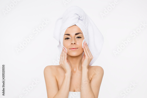 Removing makeup. Beauty and spa. A beautiful smiling woman with a towel on her head moisturizes or cleanses her face from makeup using cotton pads. Cosmetology. Women Health