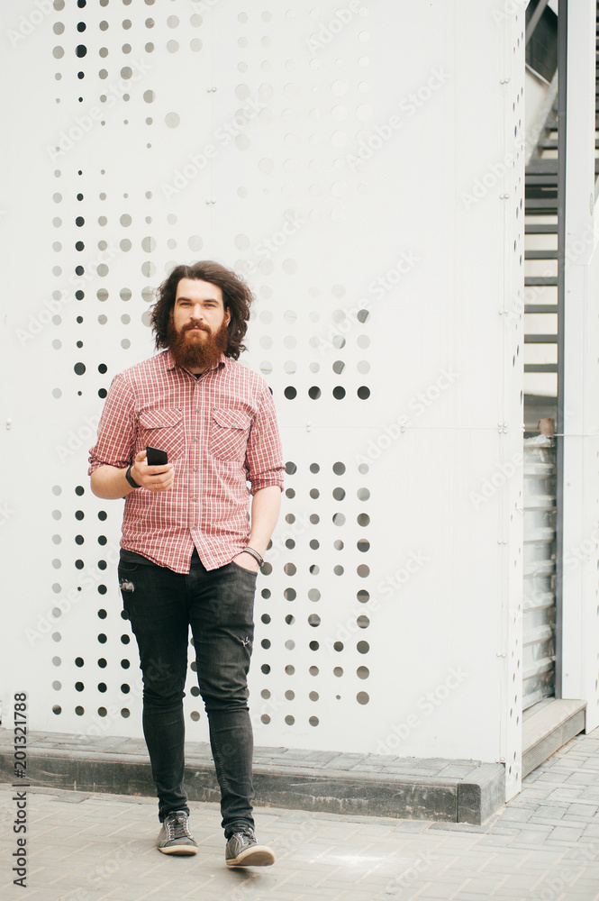 Full length portrait of bearded hipster man walking and holding mobile