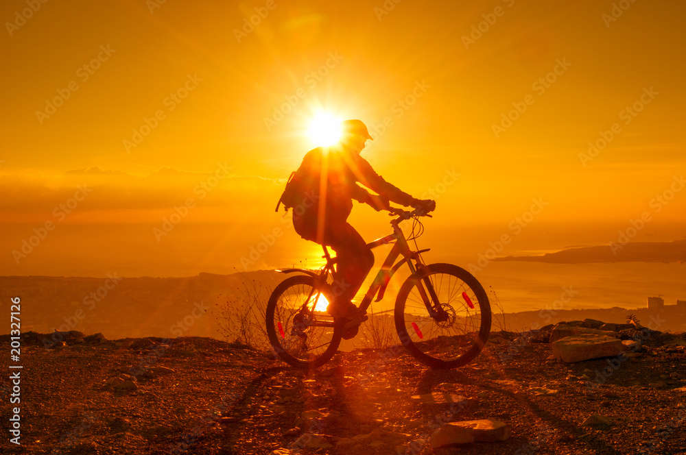 Fototapeta premium Silhouette of cyclist riding on a bike in mountain at sunset
