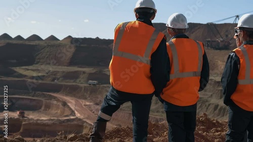 Panorama shot of a group of workers in overalls actively speaking on board a bauxite quarry.