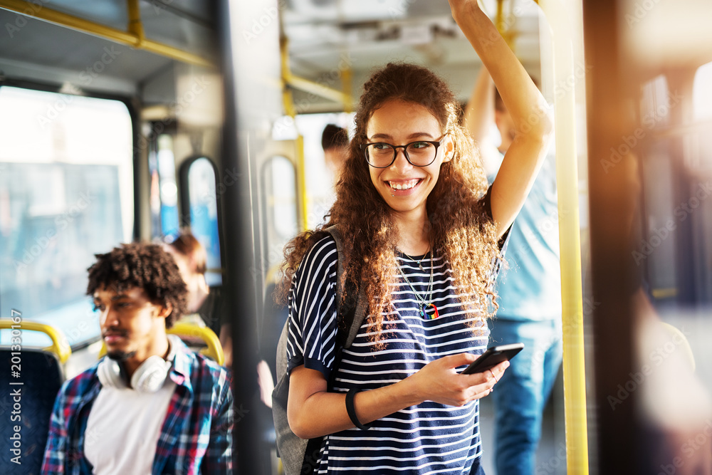 Photos Young gorgeous cheerful woman is standing on the bus using the phone and smiling